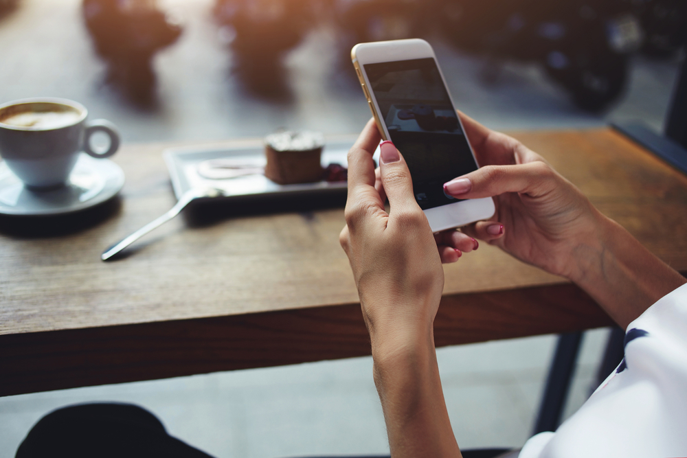 Frau hält Smartphone am Kaffeetisch